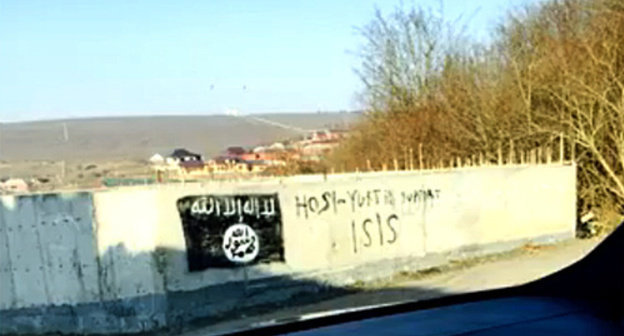 An image of the flag used by the militants of the "Islamic State" (recognized on December 29, 2014, by the Supreme Court of the Russian Federation as a terrorist organization) on a wall of the building in the village of Khosi-Yurt. Photo: screenshot of a video ISIS in Khosi-Yurt / IG in Chechnya, http://www.youtube.com/watch?v=n2sVCqLfPp0
