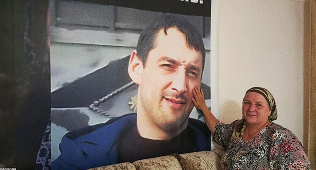 Eset Umarova next to a portrait of her son Movsar: photo: https://t.me/no_torture/3635.