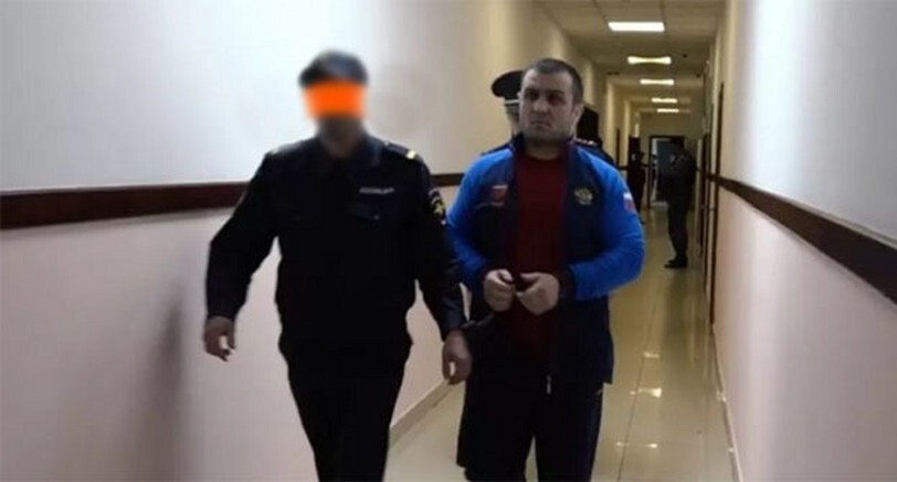 Security forces are leading Islam Atavov. Photo: "Chernovik" (the security force's face is retouched in the original publication https://chernovik.net/news/atavov-dayot-ne-sovsem-pravdivye-pokazaniya-i-vygorazhivaet-sebya-roditeli-ubitogo-v-sovetskom)