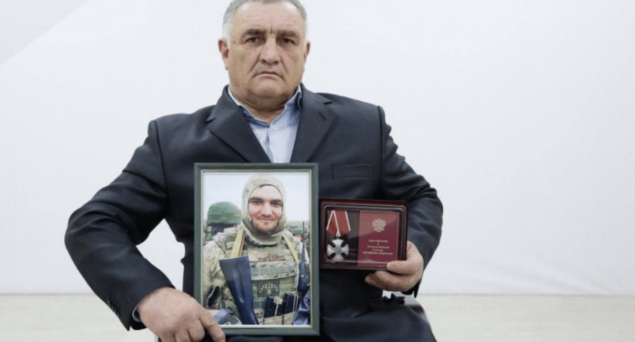 Ramazan Aripshev's father with his son's portrait and award. Screenshot of a photo from the Telegram channel of the Defenders of the Fatherland Foundation in Kabardino-Balkaria from 04.08.25, https://t.me/fond_ZO_kbr/7081.