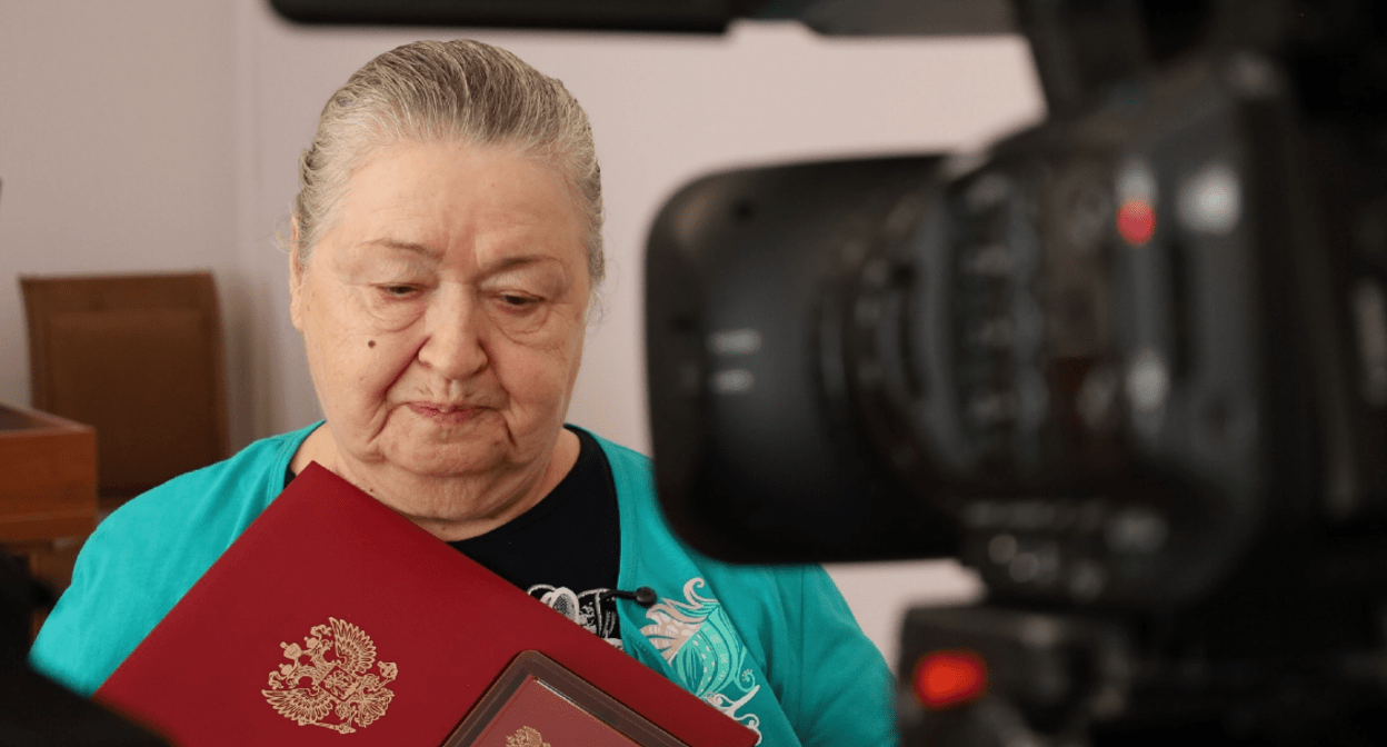 Mother of one of the fighters with her son's award. Screenshot of the photo of the Takhtamukaysky district administration from 20.08.25, https://t.me/tahtamukay/11446.