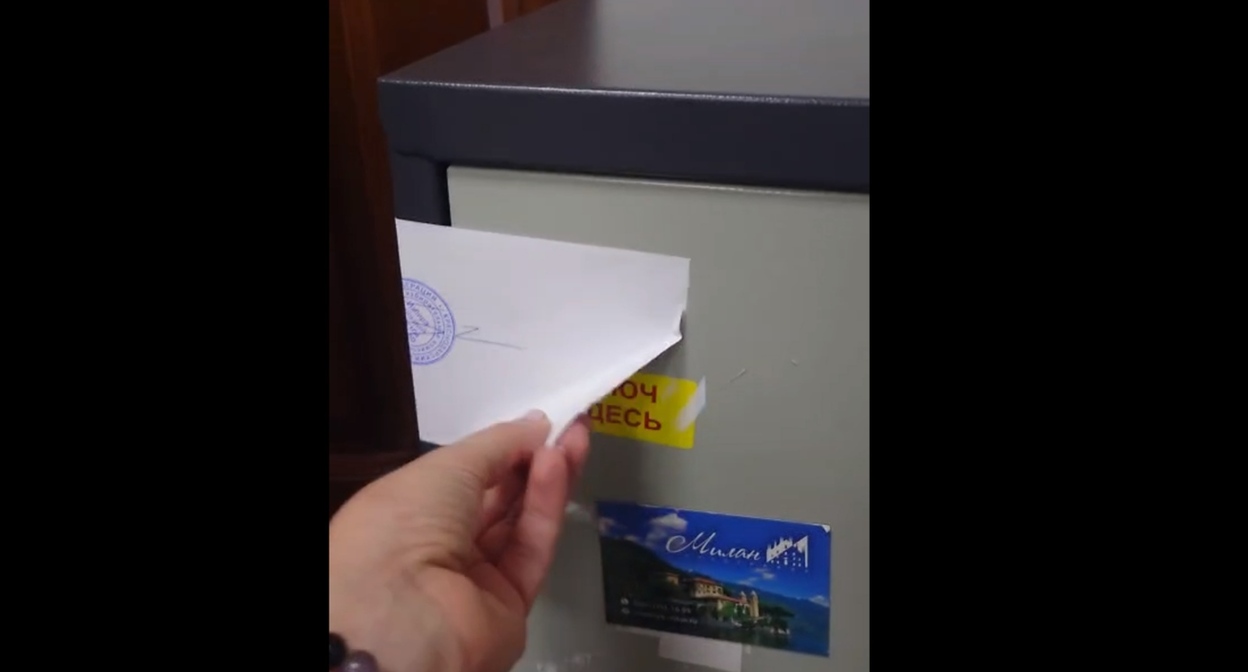 The author of the video demonstrates the peeled corner of the paper that seals the safe. Frame from the video of the Telegram channel "TIK Western Voting 2026" https://t.me/tikzapad/91