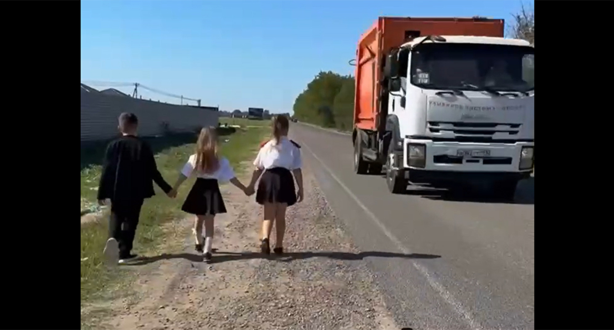 Children walk along the edge of the road due to the lack of a sidewalk. Frame from the video https://t.me/tipichkras/83286 Children walk along the edge of the road due to the lack of a sidewalk. Frame from the video https://t.me/tipichkras/83286
